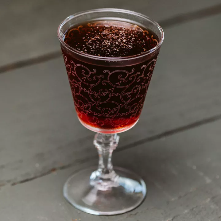 一种深宝石红色的鸡尾酒，顶部是磨碎的肉豆蔻，并在刻有华丽雕刻的尼克和诺拉玻璃杯中。